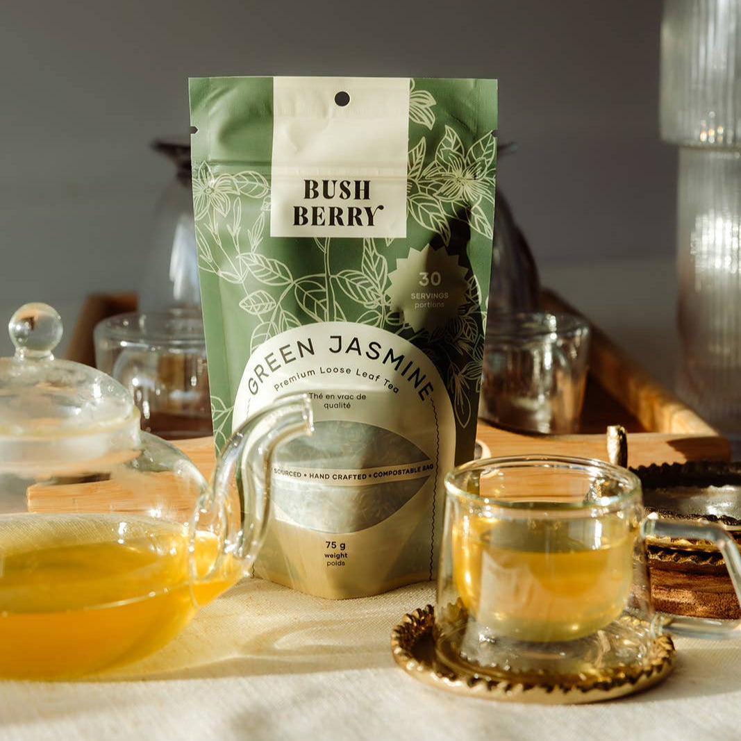 Tea packaging with 'Bush Berry' and 'Green Jasmine' on a tea tray with cups and a teapot.